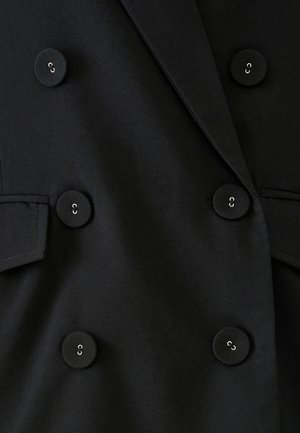 Zwarte dubbelader blazer met grote ronde knopen. Heeft een gladde textuur, scherpe revers en zijzakken.