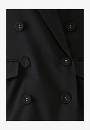 Musta kaksirivinen bleiseri suurilla pyöreillä nappeilla. Siinä on sileä pinta, terävät kaulukset ja sivutaskut.