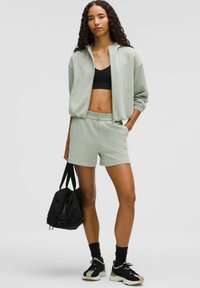 Vihreä ryppyinen cropped-vetoketjhoodie, jossa on joustavat hihat, yhteensopivat shortsit, musta urheiluliivi ja musta kuntosalilaukku. Rakeinen kangas ja rento istuvuus.