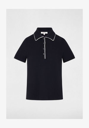 Polo nera a maniche corte con rifiniture bianche smerlate lungo il colletto e la patta dei bottoni, con quattro bottoni neri sul davanti.