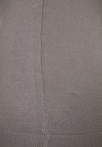 Tissu gris tricoté à texture lisse, avec une couture centrale et un ourlet côtelé. La surface présente de subtiles variations de couleur.