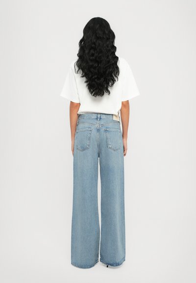 Jean large bleu clair en denim, avec une taille haute, deux poches arrière et une coupe décontractée, associé à un t-shirt blanc basic.