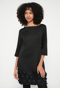 Μαύρο φόρεμα με μανίκια 3/4, με εφαρμοστό μπούστο και υφασμάτινα διακοσμητικά λουλούδια στο τελείωμα. Λείο ύφασμα με στρογγυλή λαιμόκοψη.