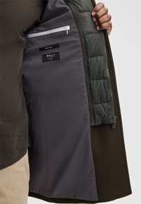 Donkergroene wolmix jas met een grijze voering, een ritszak en een gevoerd olijf paneel. Het label geeft "FINDEST WOOL" en "BALLI" aan.
