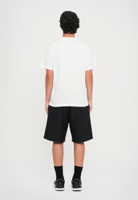 Balts īsām piedurknēm krekls ar apaļu kakla izgriezumu apvienots ar melniem šortiem. Apģērbs ir ar brīvu piegriezumu un ikdienišķu dizainu.