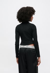 Μαύρο μακρυμάνικο τοπ με ριγέ υφή και υψηλό λαιμό, σε cropped σχεδιασμό. Συνδυασμένο με μαύρο σατέν παντελόνι με λευκή branded μέση.