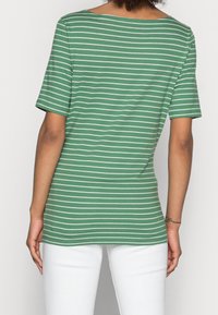 Camiseta verde a rayas con rayas horizontales blancas, de mangas cortas y escote amplio. La tela parece suave con un ajuste holgado, combinada con pantalones blancos.