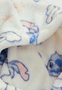 Biały polarowy koc z kolorowymi wzorami postaci z kreskówek, miękka tekstura i lekki połysk, z niebieskimi i różowymi akcentami.