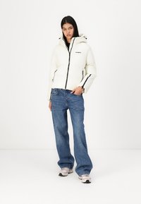 White puffer jacket with a hood, featuring a front zipper, black accents, and side pockets. Paired with blue wide-leg jeans and sneakers.