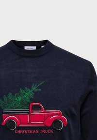 Navy trui met een geborduurde rode vintage truck die een boom vervoert, met de tekst "KERSTTRUCK" in het rood eronder. Zachte gebreide textuur.