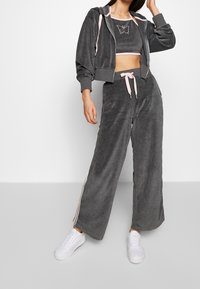 Chándal de terciopelo gris que incluye una chaqueta corta con cordones rosas y pantalones anchos a juego con rayas laterales.