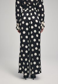 Zwarte wijde broek met grote witte stippen; zachte stof met een gladde textuur; elastische tailleband; afgewerkt met stijlvolle boorden.