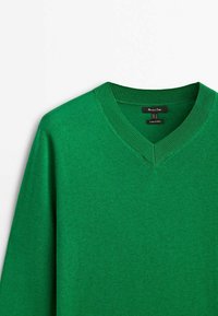 Vihreä V-pääntie villapaita, joka on valmistettu pehmeästä materiaalista. Siinä on ribbitoidut hihansuut ja kaula-aukko. Tasainen pinta ilman näkyviä kuvioita tai koristeita.