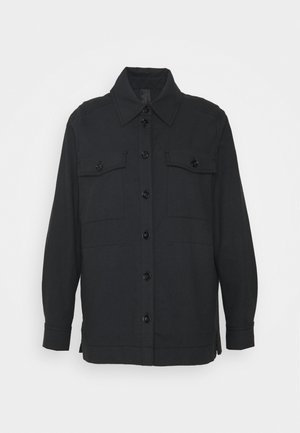 Sort langærmet jakke med knapper og to brystlommer med klapper samt krave, vist mod en ensfarvet lys baggrund.