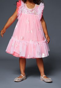 Růžové tylové šaty se flitrovaným korzetem, volánkovými rameny a metalickými srdcovými vzory. Kombinované s třpytivými stříbrnými balerínami.