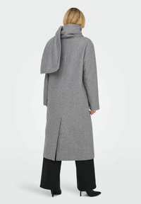 Lungo cappotto grigio in misto lana, con colletto alto e spacco sul retro. Abbinato a pantaloni larghi neri e stivali con tacco alto.