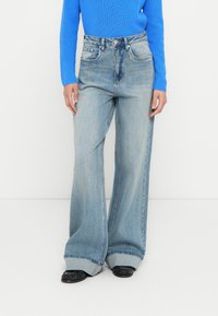 Light blue wide-leg jeans made of denim, featuring five pockets, a high waist, and a turned-up hem. Paired with a long-sleeve blue top.