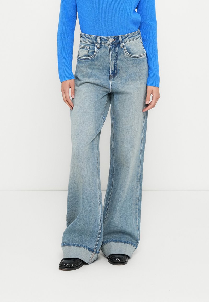 Light blue wide-leg jeans made of denim, featuring five pockets, a high waist, and a turned-up hem. Paired with a long-sleeve blue top.