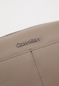 Beżowy skórzany portfel z fakturowaną powierzchnią, widocznymi szwami oraz delikatnie wytłoczonym logo Calvin Klein z przodu.