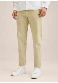 Beige puuvillakankaiset chinot suoralla lahkeella, joissa on etutaskut ja siisti muotoilu. Yhdistetty valkoisiin tennareihin ja valkoisiin sukkiin.