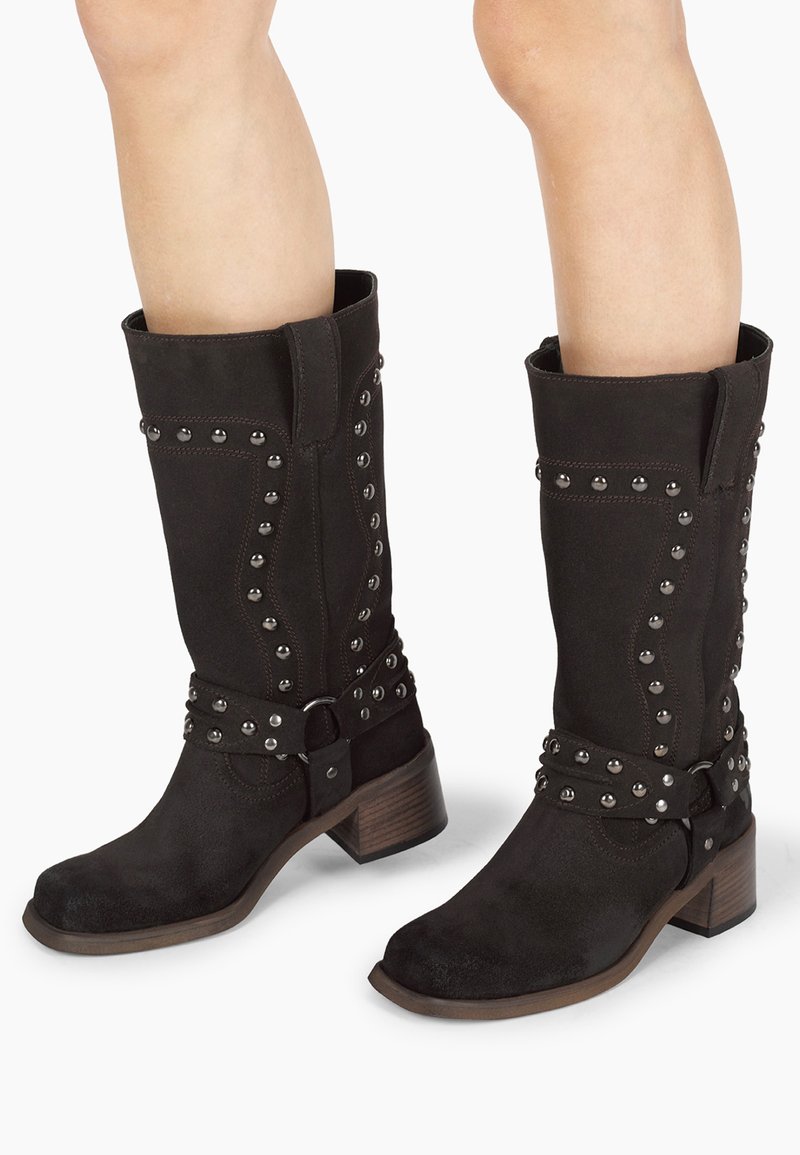 Stivali neri in suede alti fino al ginocchio con borchie argentate lungo il lato e una fascia con fibbia, caratterizzati da un tacco in legno stratificato.