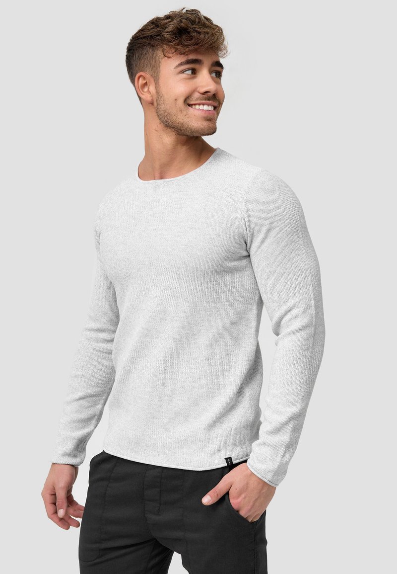 Lichtgrijze gebreide t-shirt met lange mouwen, ronde halslijn en een textiele stof. Gepaard met zwarte broek, met een klein label aan de zoom.