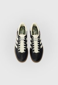 Schwarze und cremefarbene Sportschuhe mit einer strukturierten Oberseite, drei weißen Streifen und einer gemusterten Innensohle. Gummisohle mit einem klassischen Design.