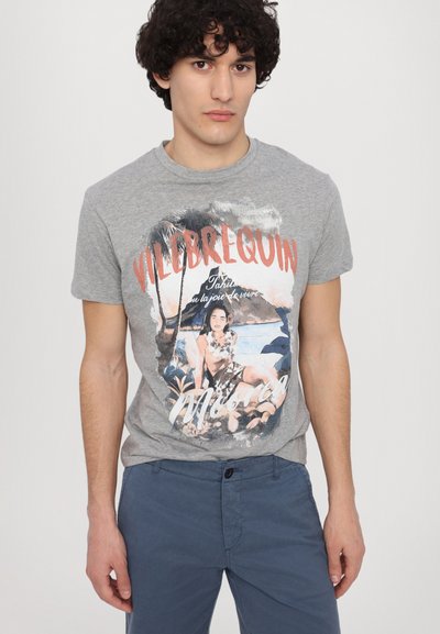 Camiseta de algodón gris con un colorido estampado gráfico de temática playera y el nombre de la marca "Vilebrequin" en rojo, combinada con pantalones azul marino.