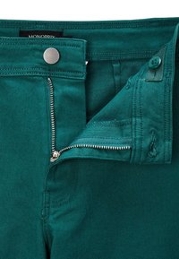 Pantalons bleu foncé en teal avec une fermeture éclair argentée, une fermeture à bouton et des coutures détaillées ; fabriqués en tissu texturé et durable.
