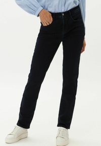 Dunkelblaue Jeans mit schmaler Passform, aus Baumwollmischgewebe gefertigt. Verfügt über Fronttaschen und einen Knopfverschluss, kombiniert mit weißen Sneakers.