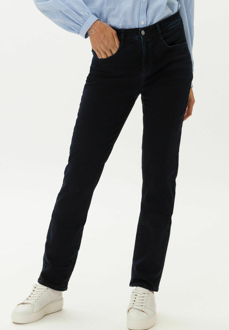 Dunkelblaue Jeans mit schmaler Passform, aus Baumwollmischgewebe gefertigt. Verfügt über Fronttaschen und einen Knopfverschluss, kombiniert mit weißen Sneakers.