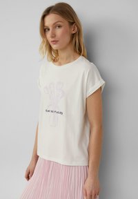 T-shirt blanc à manches courtes avec un design de vase de fleurs lavande et le texte "RUE DES FLEURS". Assorti à une jupe plissée rose. Matière en coton douce.