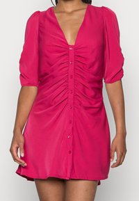 Fuchsia klänning med djup V-ringning, korta puffärmar, knappstängning och rynkning fram. Lättviktsmaterial med en mjuk yta.