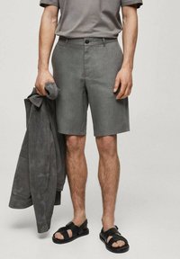 Shorts gris en tissu léger, dotés d'une coupe ajustée et d'une fermeture à bouton. Associés à une chemise grise assortie et des sandales noires.