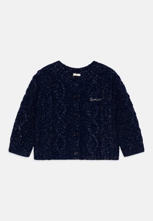 Donkerblauwe gebreide cardigan met een kabelbrei patroon, ronde hals, lange mouwen en vijf zwarte knopen aan de voorkant. Kleine geborduurde tekst.