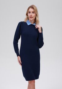 Robe tricotée bleu marine avec des manches longues et une silhouette ajustée ; présente un col rayé bleu clair. Texture lisse avec des accents côtelés aux poignets et à l'ourlet.