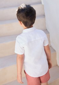 Chemise blanche à manches courtes avec col, vue de dos, associée à un short rose clair. Aucun motif ou accent visible.