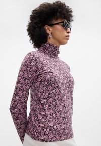 Top de cuello alto de manga larga en púrpura oscuro con un patrón floral rosa. Cuenta con un cuello alto y un diseño ajustado. Textura de tela suave.