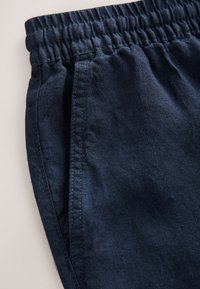 Marineblaue Leinenhose mit elastischem Bund und Seitentaschen, sichtbaren Nähten und glatter Textur.