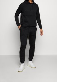 Ensemble sweat à capuche et joggers noirs en matière douce, doté d'une poche avant et d'un cordon de serrage. Rehaussé d'un logo discret sur la poitrine.