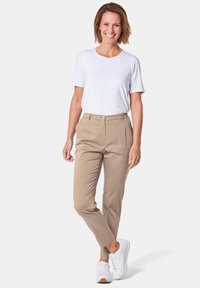 Pantalons beiges ajustés et un t-shirt blanc uni, associés à des baskets blanches. Les pantalons présentent une poche avant et une fermeture à bouton.