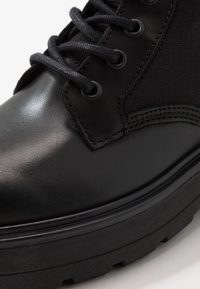 Schwarze Stiefel mit einer glatten Lederoberfläche und Stoffakzenten. Dicke schwarze Sohle mit strukturiertem Muster und schwarzen Schnürsenkeln.