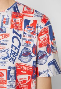 T-shirt à manches courtes couleur crème avec un imprimé rétro coloré comportant le logo Iceberg en bleu, rouge et blanc, ainsi que des illustrations vintage de nourriture.