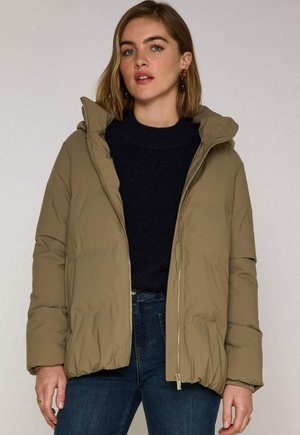 Khakifarbene Steppjacke mit Reißverschluss, Kapuze und elastischen Bündchen, kombiniert mit einem dunklen Pullover und blauen Jeans. Glatte Textur und leicht.