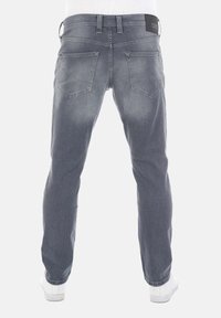 Widok z tyłu osoby noszącej wyblakłe szare dżinsy z tylnymi kieszeniami i białe sneakersy na jednolitym tle.