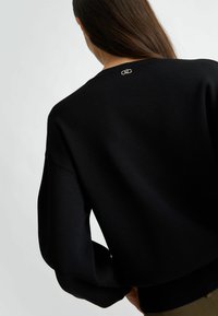 Pullover nero a maglia con scollo rotondo e spalle scese. Presenta un logo ricamato discreto sul retro, una texture liscia e un fit rilassato.
