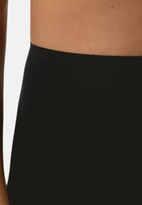 Svart tygmidja på leggings, mjuk textur. Slät yta utan mönster som bildar en oavbruten linje mot huden.