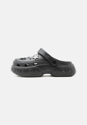 Μαύρο clog τύπου slip-on με παχιά σόλα, οπές αερισμού, ρυθμιζόμενο λουράκι στη φτέρνα και δύο ασημένια κρεμαστά σε σχήμα αστεριού στην κορυφή.
