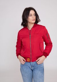 Rote Bomberjacke aus einem glatten Stoff, mit gerippten Bündchen und einem Frontreißverschluss. Zwei Seitentaschen und eine Armtasche sind sichtbar.