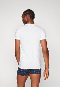 T-shirt blanc à manches courtes avec un col rond ; porté avec un boxer bleu marine à motifs comportant de petits textes et icônes blancs.